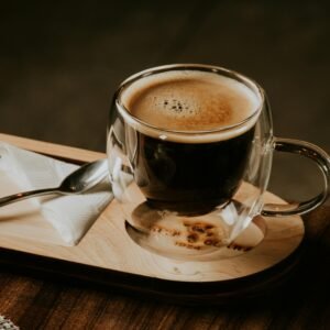 Double-walled glass mug with rich espresso on wooden tray in a cozy setting.