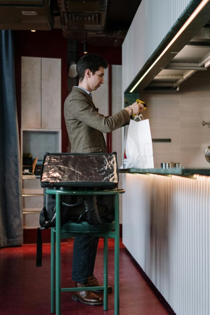 A man organizes items into a paper bag in a contemporary kitchen setting.